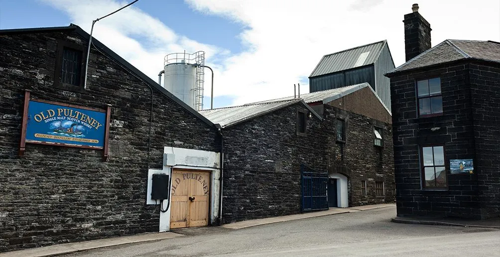 Distillery building of Old Pulteney made out of dark grey brick with a bright blue name sign attached on the wall