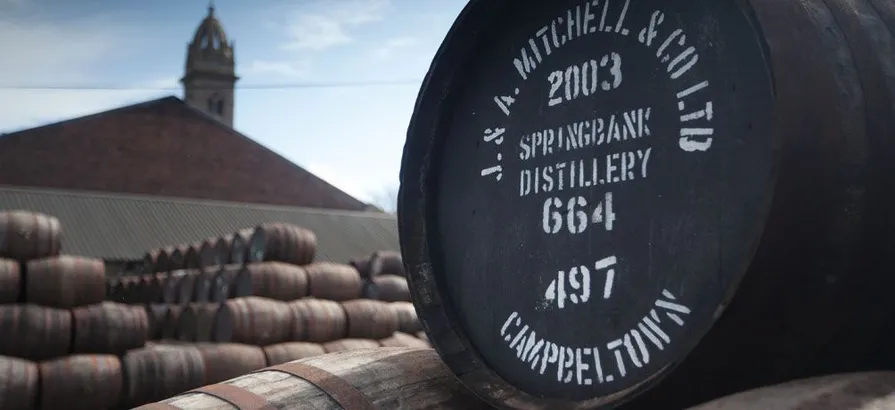 Numbered casks with distillery name and distilling year painted on their lids lying outside in rows on top of each other