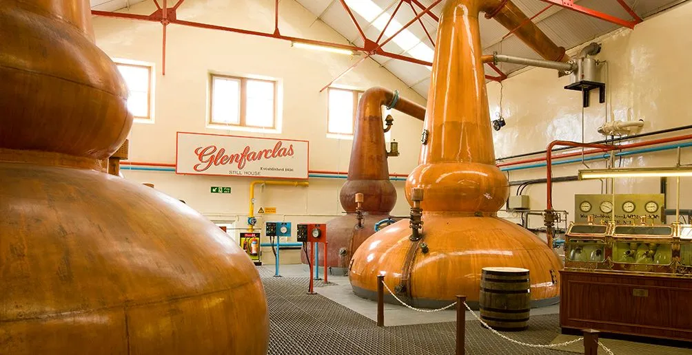 Three copper pots stills inside Glenfarclas still house with a big Glenfarclas billboard in the background