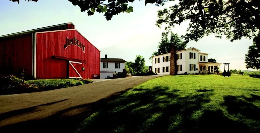 Das rote Lagerhaus von Jim Beam mit Blick auf einen grünen Rasen und ein weißes Empfangshaus ganz rechts