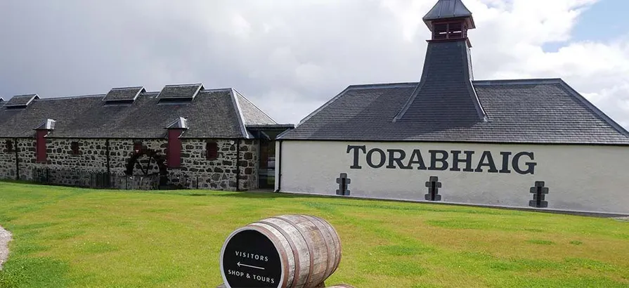 Torabhaig's distillery buildings with its name painted on the wall standing behind a cask-shaped direction sign on a green yard