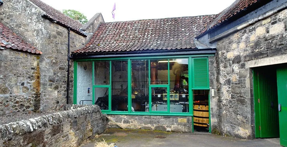 Interior of Daftmill distillery with copper pot stills and a wooden washbacks viewed from outside through a green window