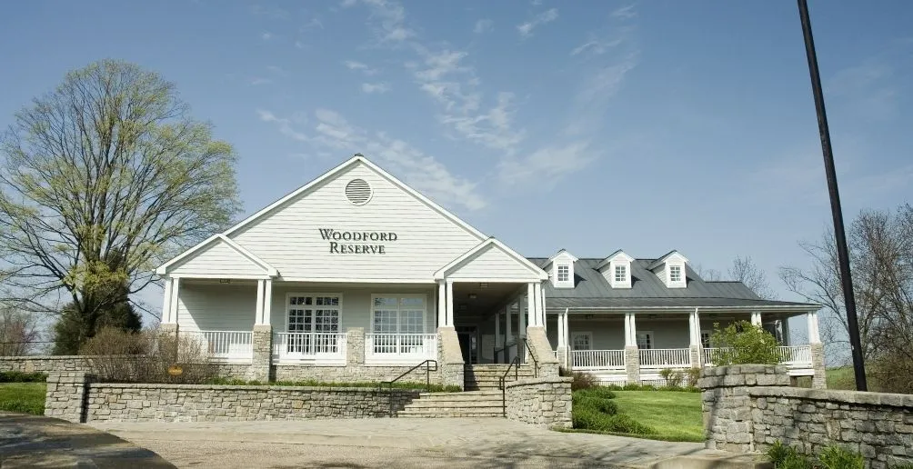 Front view of Woodford Reserve distillery surrounded by several trees on a sunny day with blue sky in the background