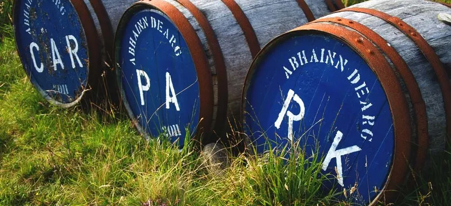 Abhainn Dearg casks lying on the grass with the distillery's name and filling dates painted on their blue lids