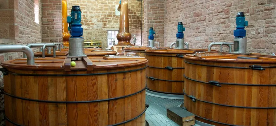 Das Innere des Destillierhauses von Annandale mit vielen hölzernen Maischebottichen in der Brennerei und einem kupfernen Pot Still im Hintergrund