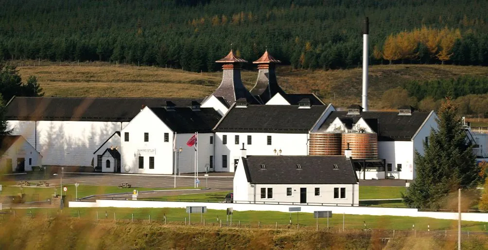 Dalwhinnie's white distillery building with a green front yard located at the foot of a green hill