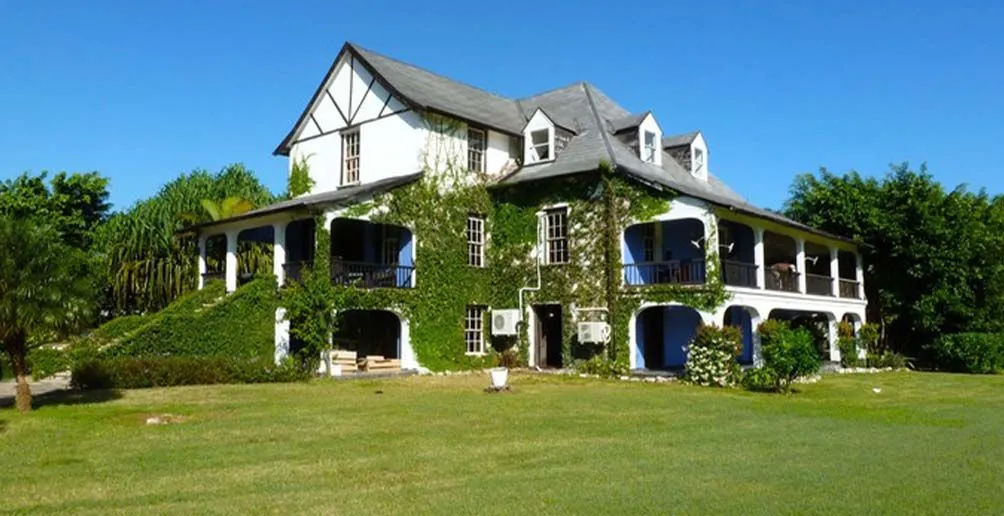 Hampden Great House with walls covered by green vines viewed from the grass yard on a nice day