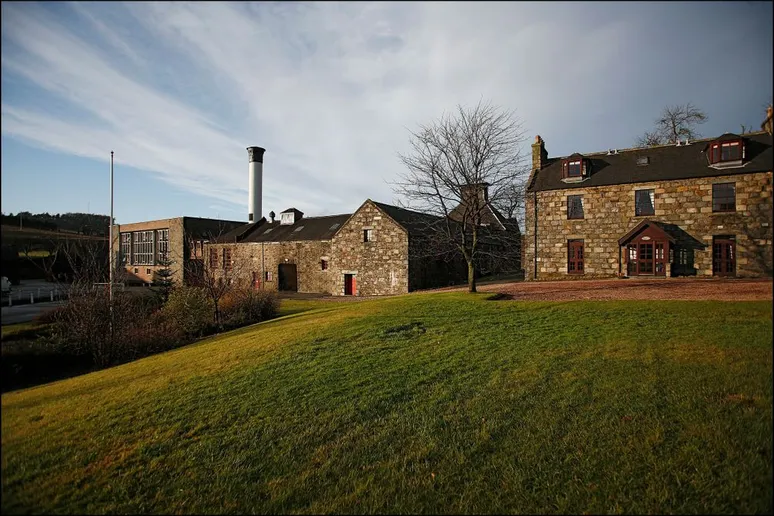 Glendronach distillery's brown brick buildings viewed from its green front yard