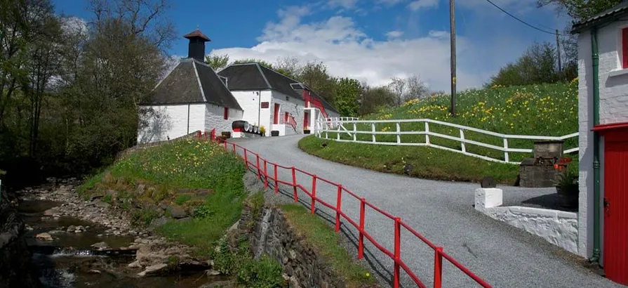 Picturesque path leading to Edradour distillery located between a stream and a mound cover in green grass