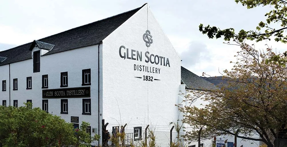 Glen Scotia's white distillery building with its name attached on the wall surrounded by green trees