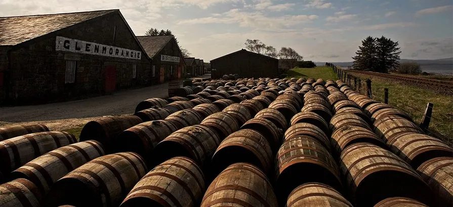 Whisky casks lying in the courtyard of Glenmorangie distillery in front of the warehouses on a cloudy day