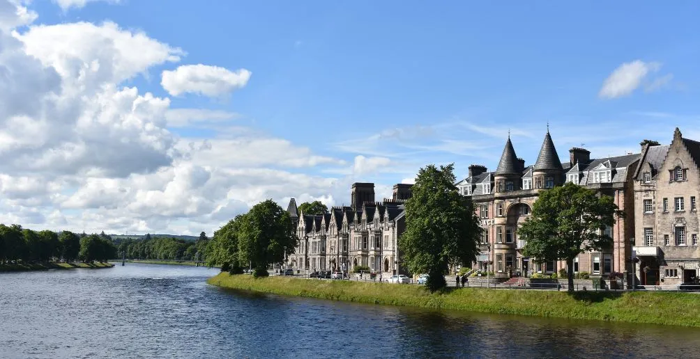 Blick auf die Stadt Inverness vom Flussufer aus mit blauem Himmel im Hintergrund