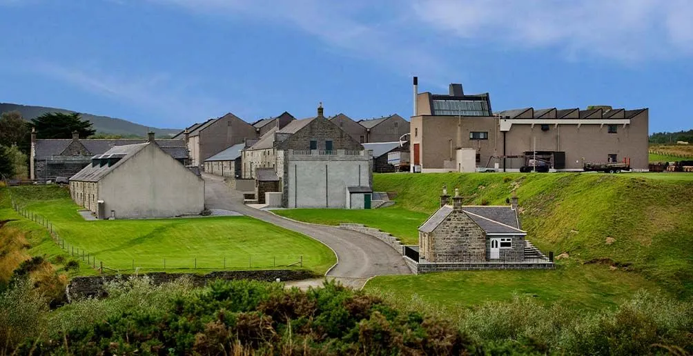 The whole Glenglassaugh distillery area surrounded by green fields with blue sky in the background viewed from afar