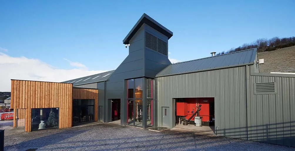 Mordern still house made of gray metal walls and glass with a reception room nearby on the right at GlenWyvis distillery