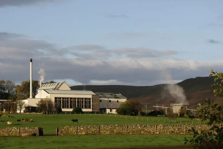 Clynelish Distillery mit einem grünen Vorgarten am Fuße eines Hügels an einem bewölkten Tag