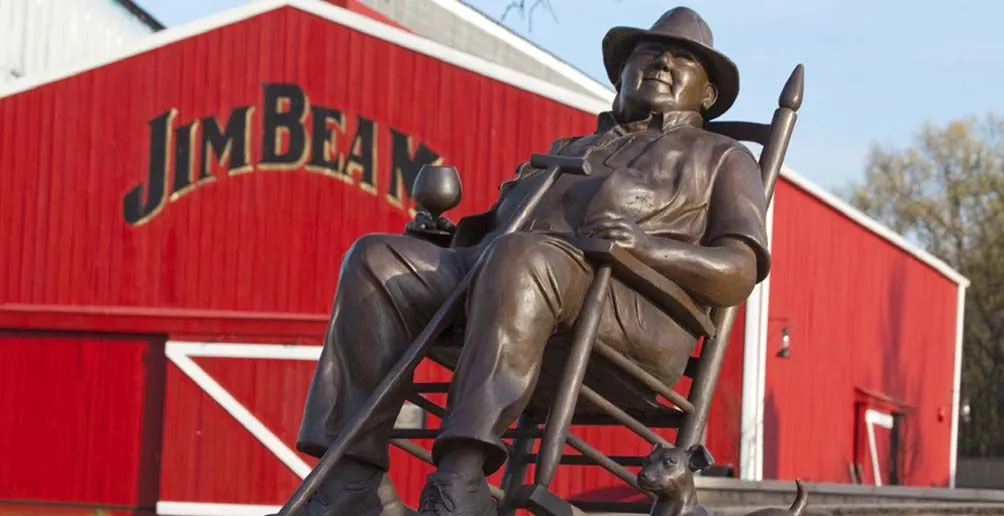 Bronze statue of Booker Noe sitting on a rocking chair in front of Jim Beam's red warehouse