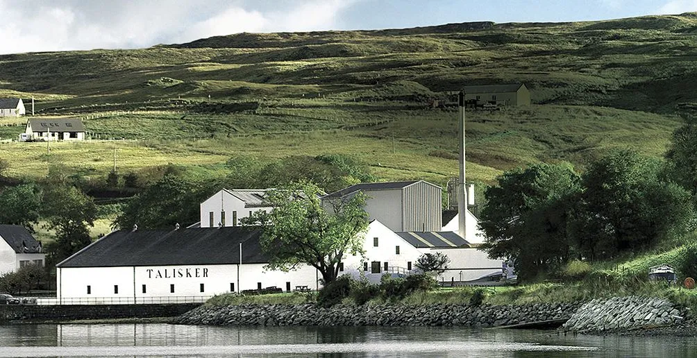Talisker distillery located at the foot of a hill hiding itself among the nature viewed from the other bank of the river