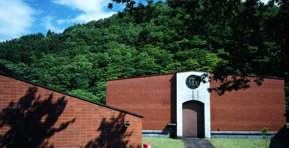 Miyagikyo's red distllery building surrounded by green nature on a sunny day