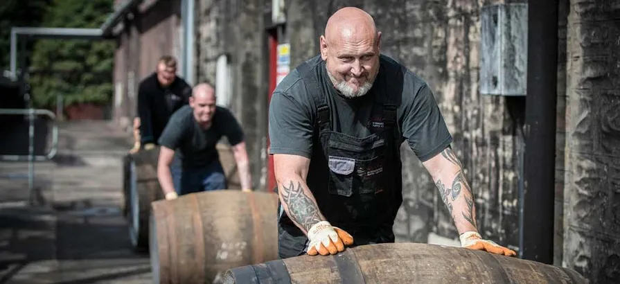 Employees at Blair Athol distillery rolling casks along a side of the warehouse