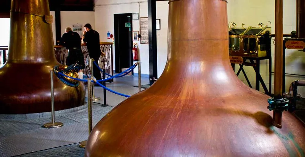 Copper pot stills inside the Arran distillery with two workers in the background