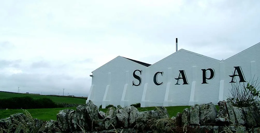Scapa distillery with its name painted on the wall located in the middle of a grass field