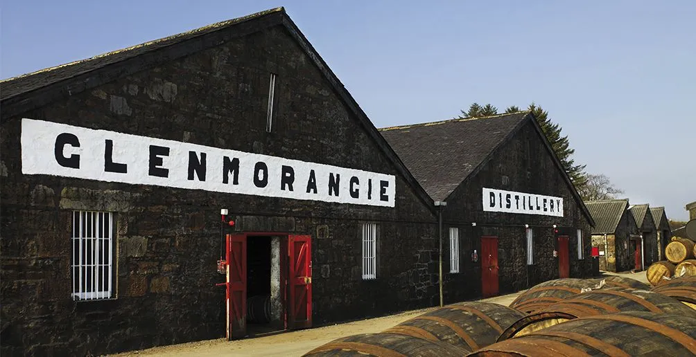 Casks lying outside in front of Glenmorangie's dunnage warehouses made of stone with its name painted on the walls