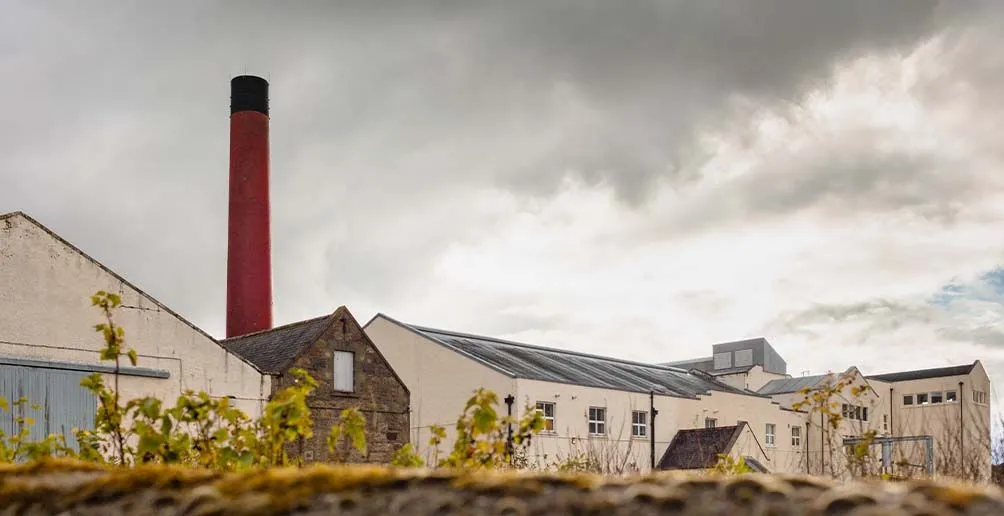 Benrinnes distillery with beige walls and a red chimney on a cloudy day