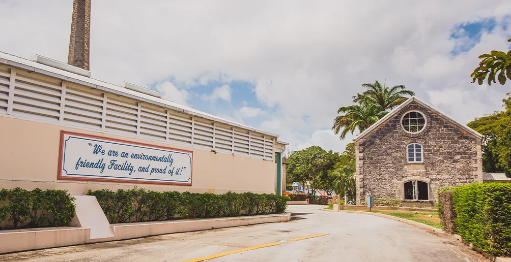 Entrance way to Foursquare distillery with its slogan on the wall of a beige building on the left and a stone reception house on the far right