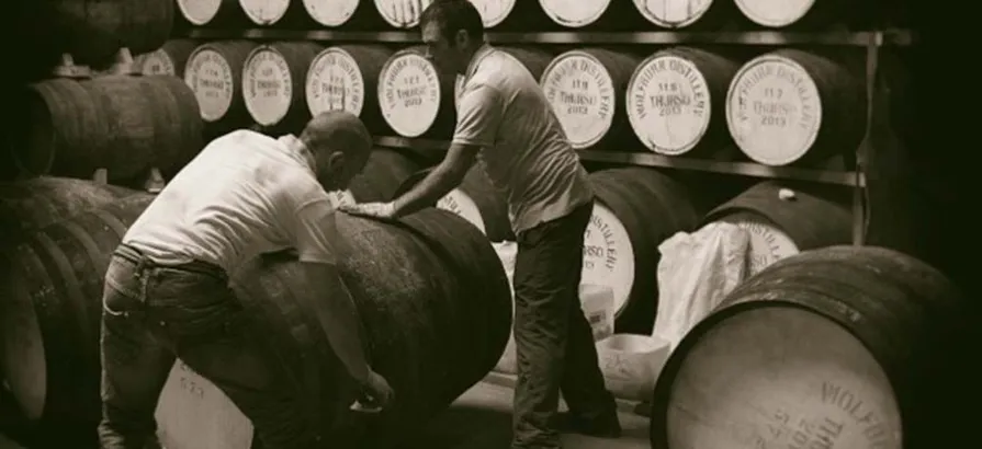 Black and white picture of two employees at Wolfburn distillery moving a cask in the warehouse