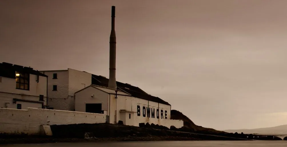 Bowmore's white distillery building with its name painted on the side wall viewed from the bay