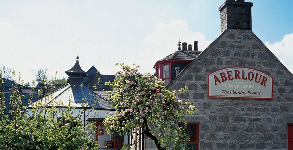 Aberlour distillery building with its extraordinary pagoda style roof surrounded by trees in full bloom on a sunny day