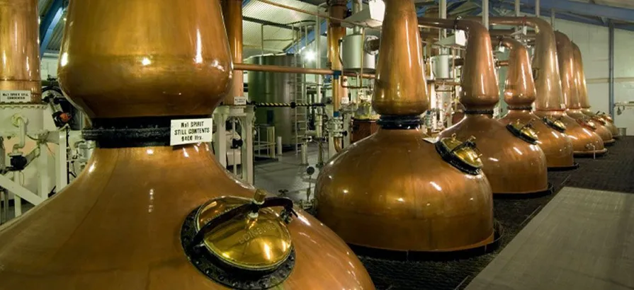 A row of seven copper pot stills inside the still house with mash tuns in the background