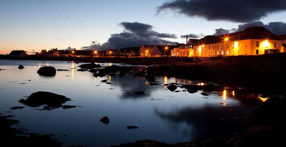 Bruichladdich distillery with lights on viewed from the bay during a low tide at sunset