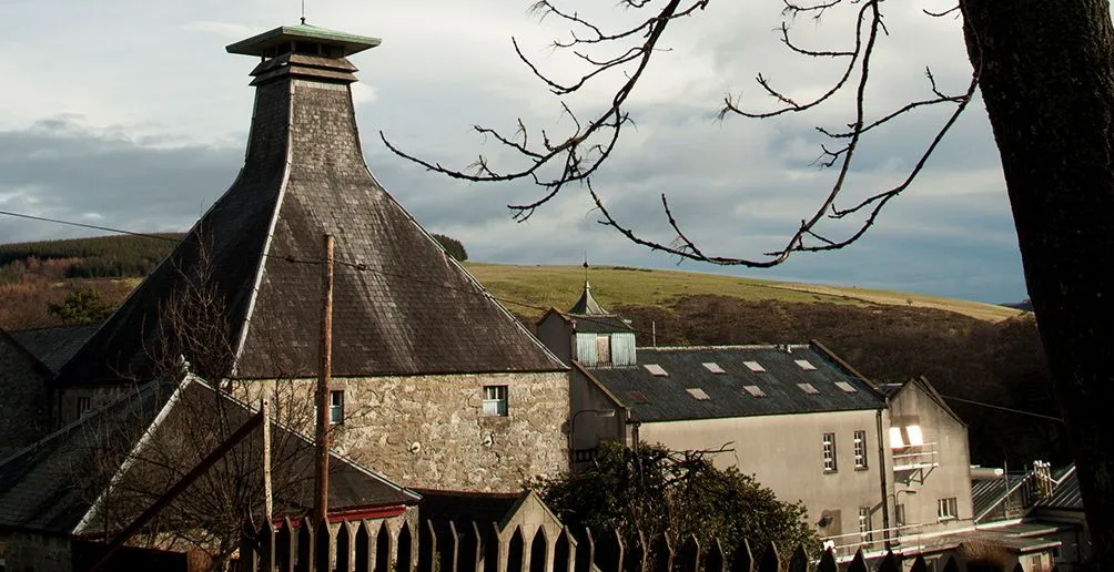 The whole Mortlach distillery area with a focus on its special pagoda rooftop viewed from behind some bare tree branches