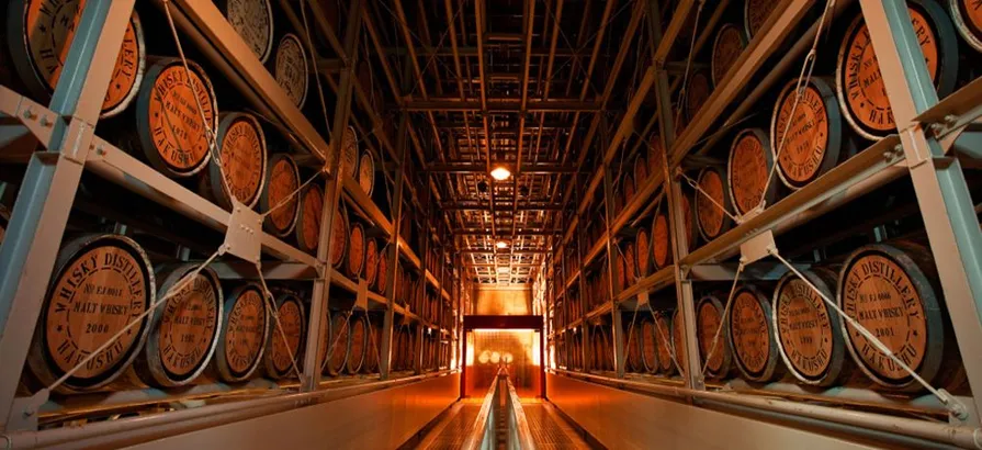 Warehouse aisle with rows of whisky casks stacked to the roof in metal shelves