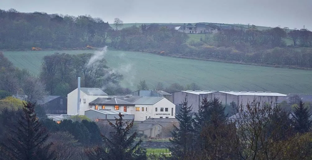 Macduff distillery located among nature covered in steam coming out from its chimney