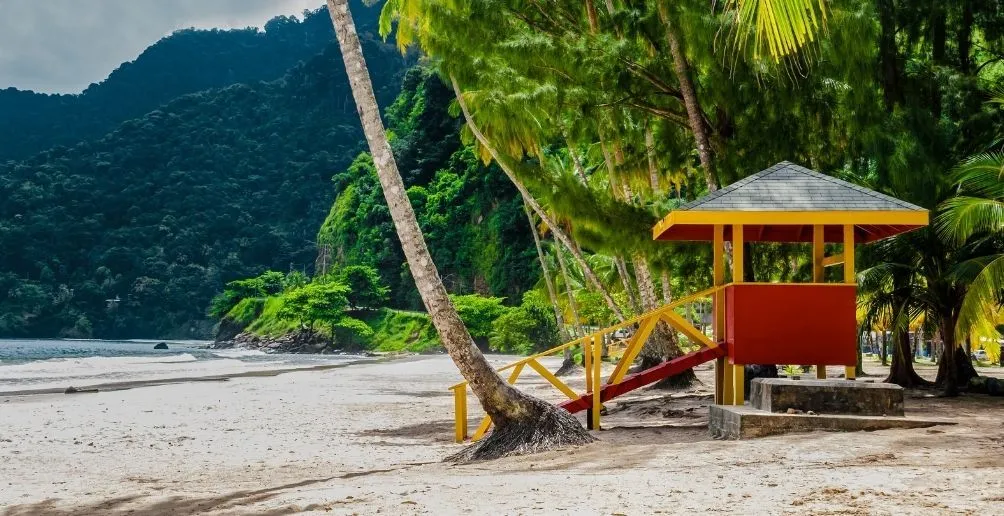 A red booth with yellow bridge located on the beach by the ocean with green palm trees and mountains in the background