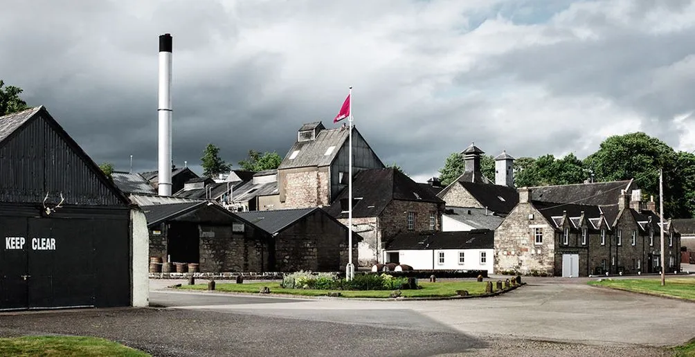 Dalmore distillery's stone buildings on a grey cloudy day viewed from the entrance path