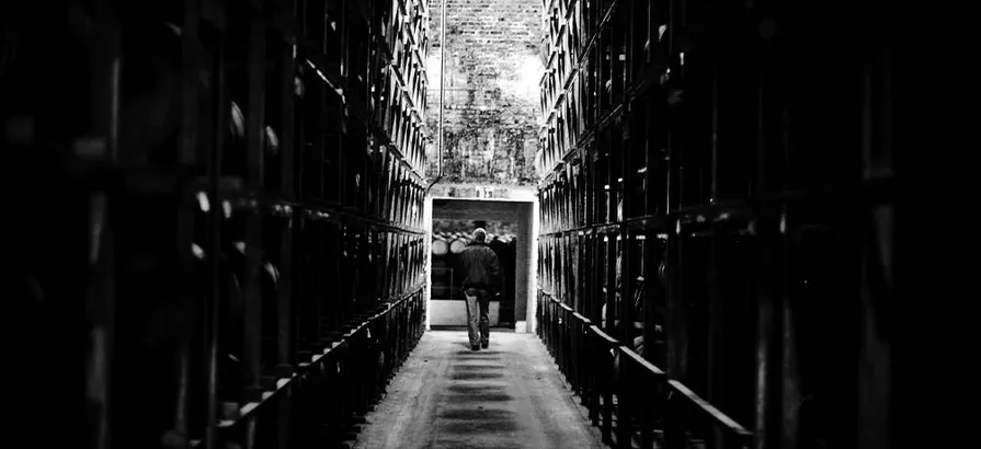 A black and white photo of an employee walking between two cask shelves in Bruichladdich's warehouse