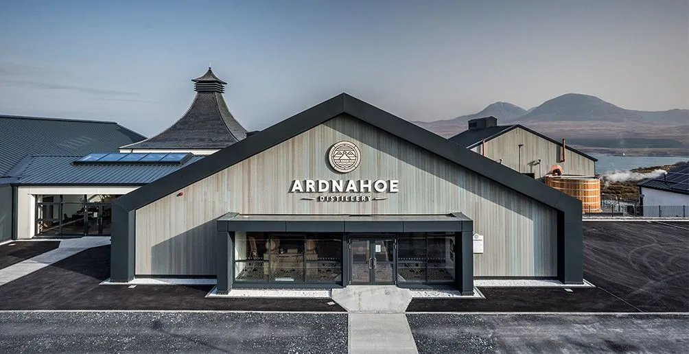 Front view of Ardnahoe distillery on the Isle of Islay with a lake and mountains behind