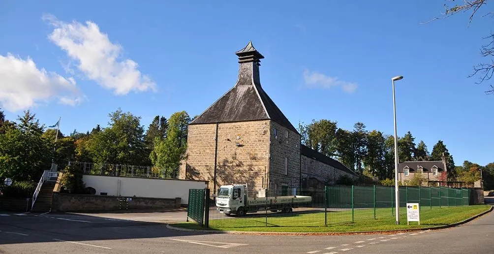 Linkwood's distillery building made of stone with its pagoda style roof with green trees in the background on a nice day