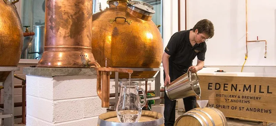 Eden Mill's employee filling a cask next to an Alembic still with two copper pot stills in the background