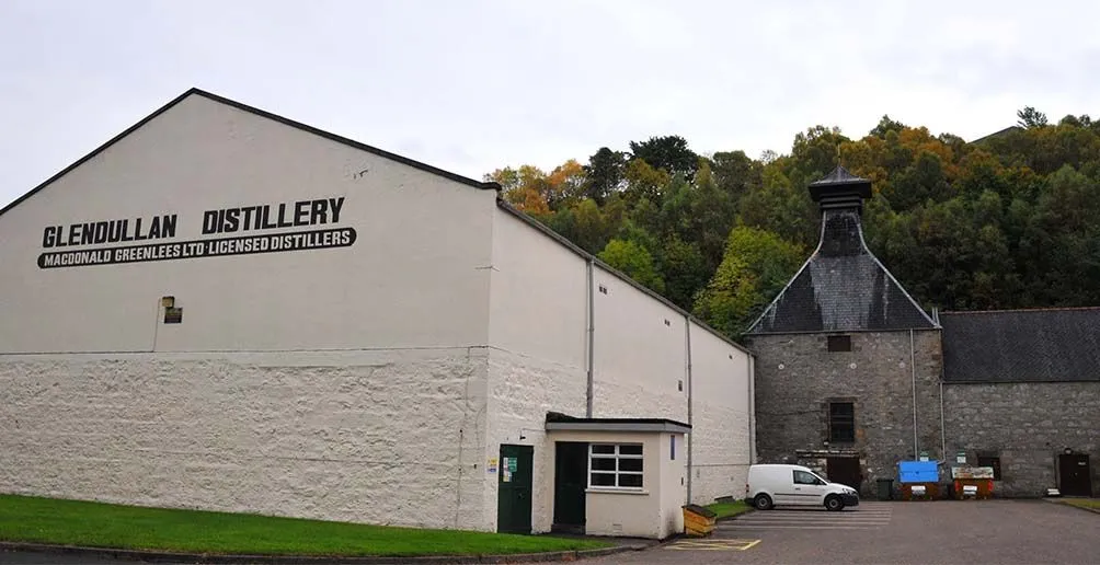 A corner of Glendullan distillery site with a white building and a warehouse made of bricks