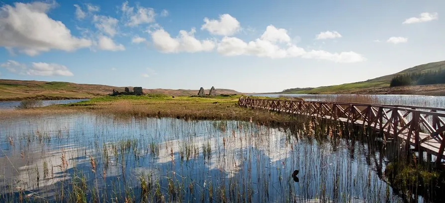 Holzbrücke, die an einem schönen Tag über einen Fluss zu einem grünen Ait in Speyside führt