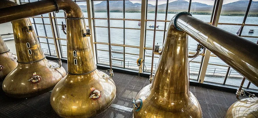 Copper pot stills of Caol Ila in the stillhouse with view on the bay