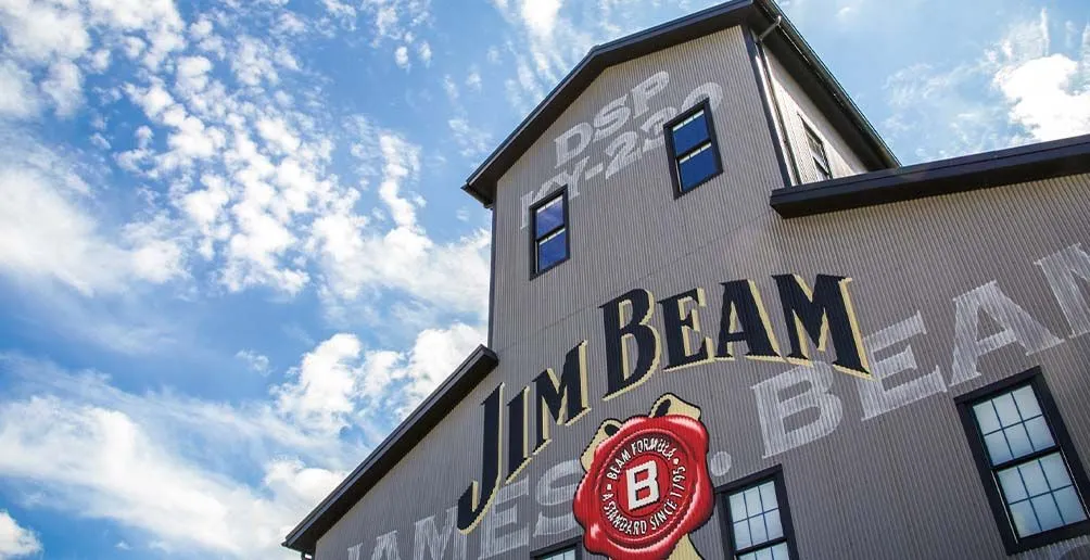Close view on Jim Beam's distillery building with its name and logo painted on the wall on a blue sky background