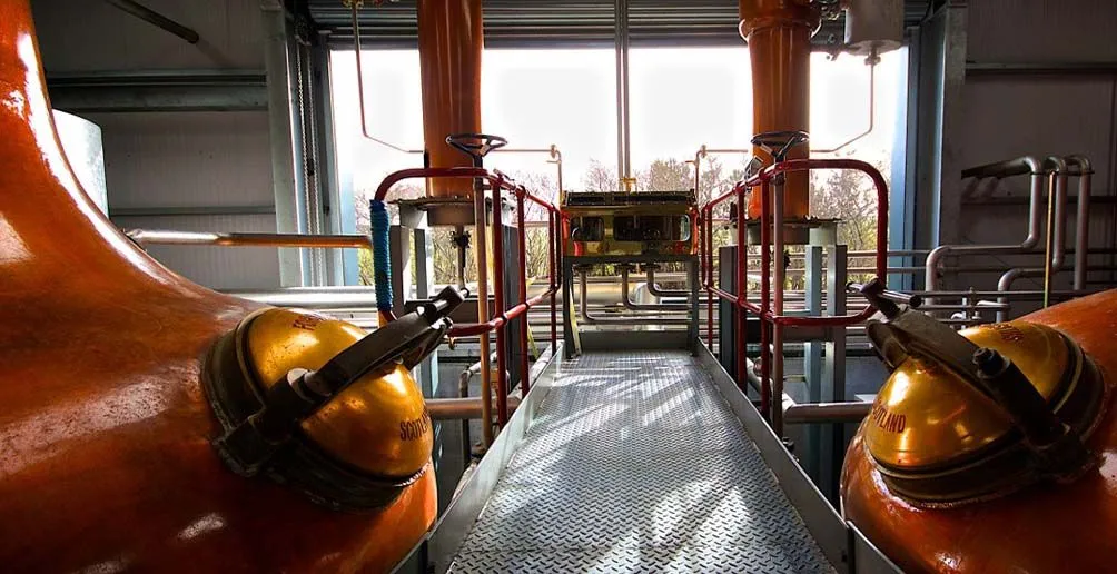 Picture of the interior of Wolfburn's still house with two copper pot still lying on two sides overlooking the outside of the distillery