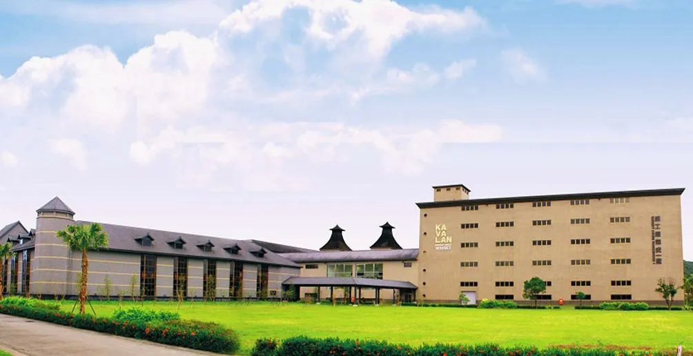 Kavalan's distillery building with beige walls located behind a green yard viewed from the entrance path