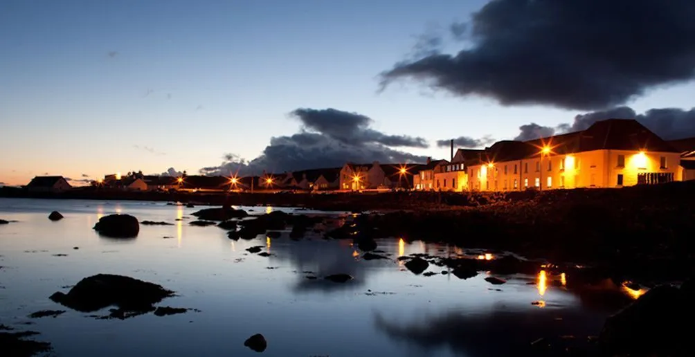 The whole Bruichladdich distillery area with lights on at sunset viewed from the bay