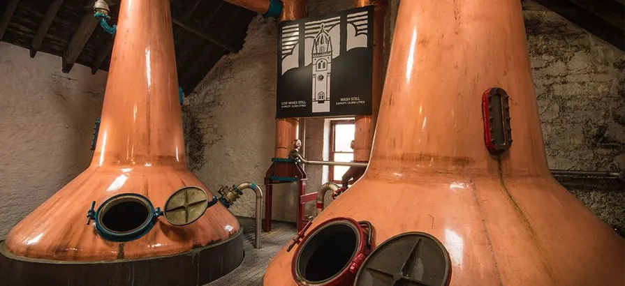 Close view on Glengyle's copper pot stills with open lids and its name sign in the background